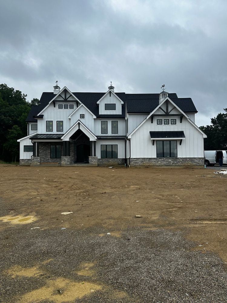 A large white house with a black roof is sitting in a dirt field.
