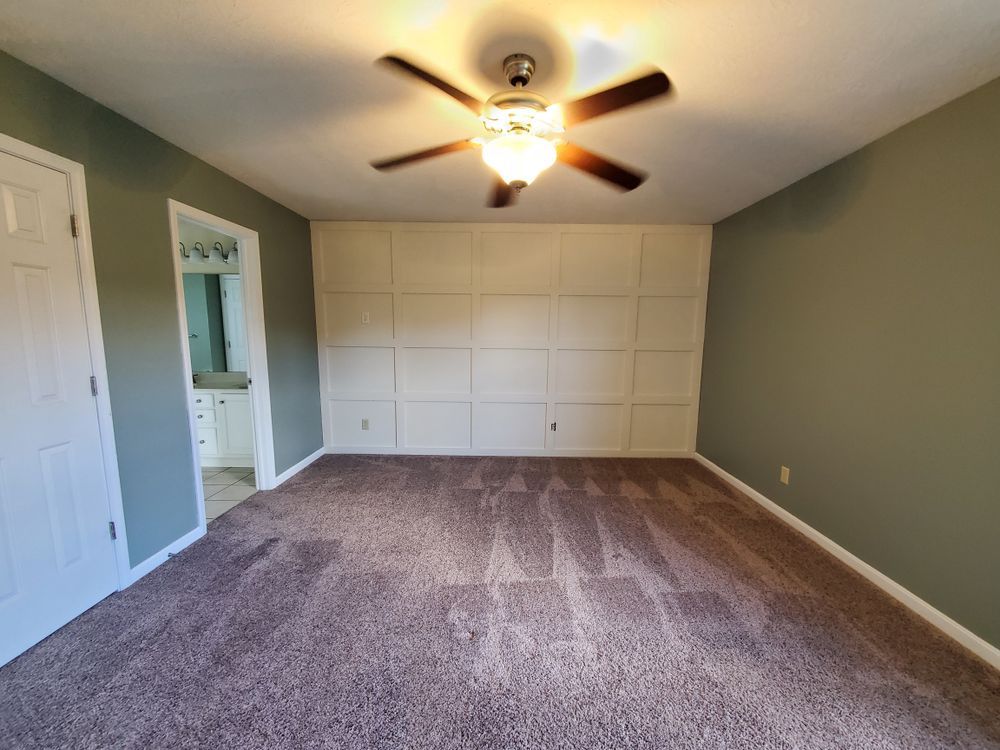 An empty bedroom with a ceiling fan and a purple carpet.