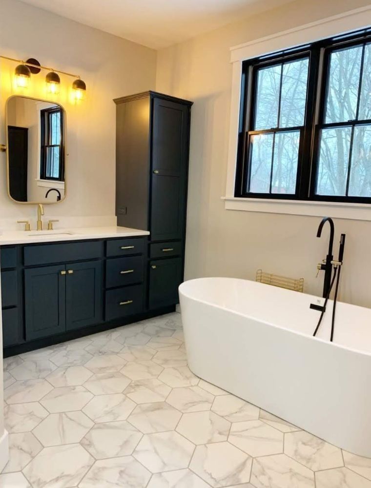 A bathroom with a tub , sink , mirror and window.
