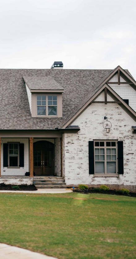 Grey stone facade home with grey garage door, brown stairs, and black front door.