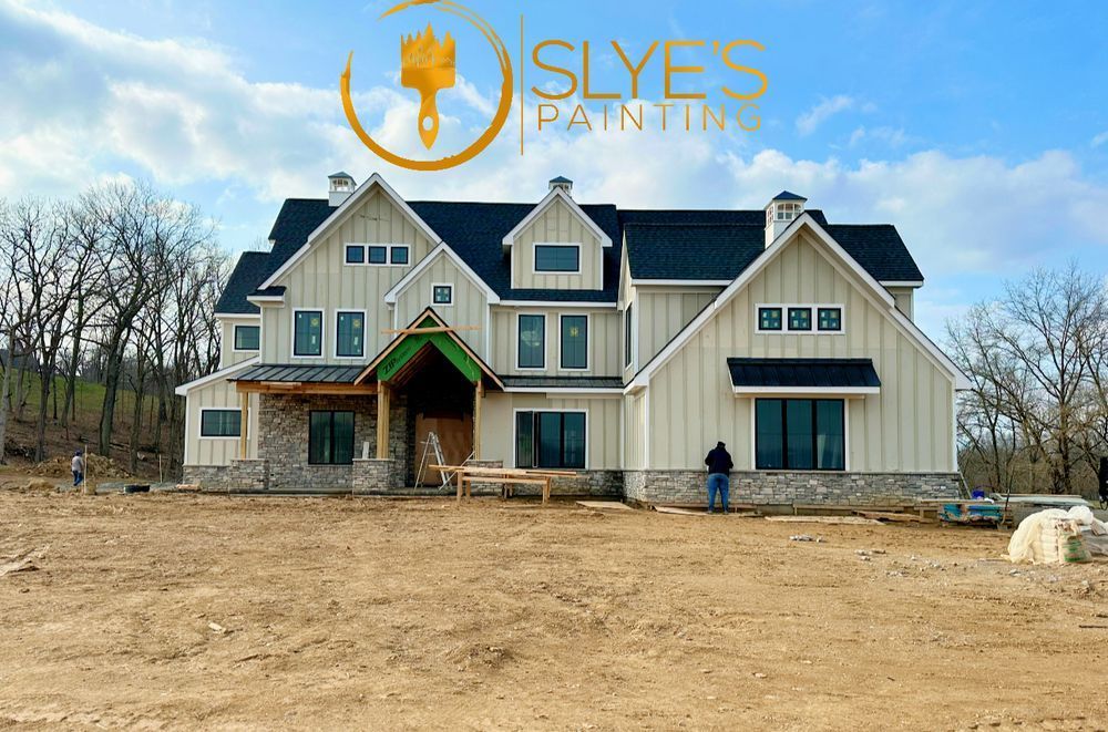 A large white house with a black roof is being painted by islyes painting