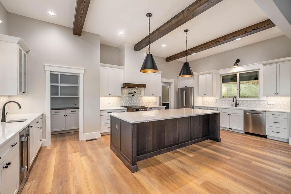 A kitchen with white cabinets , hardwood floors , stainless steel appliances and a large island.