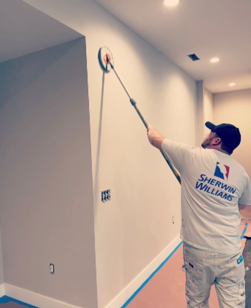 A man wearing a sherwin williams shirt is painting a wall
