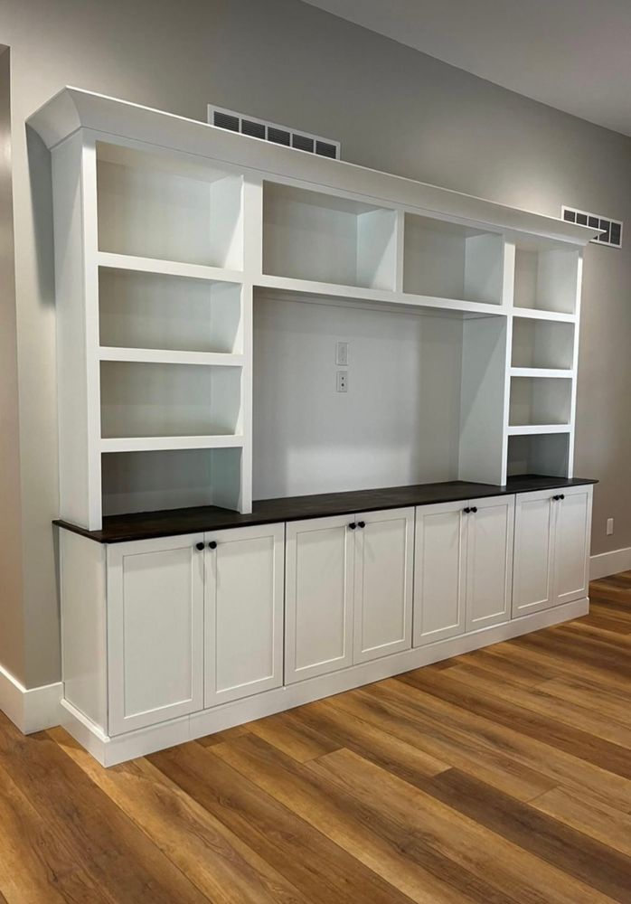 A large entertainment center with white cabinets and shelves in a living room with hardwood floors.