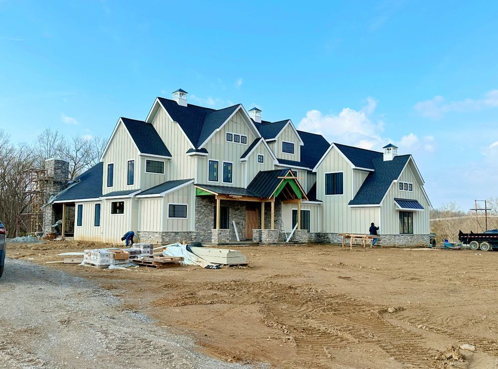 A large white house with a black roof is being built in a dirt field.