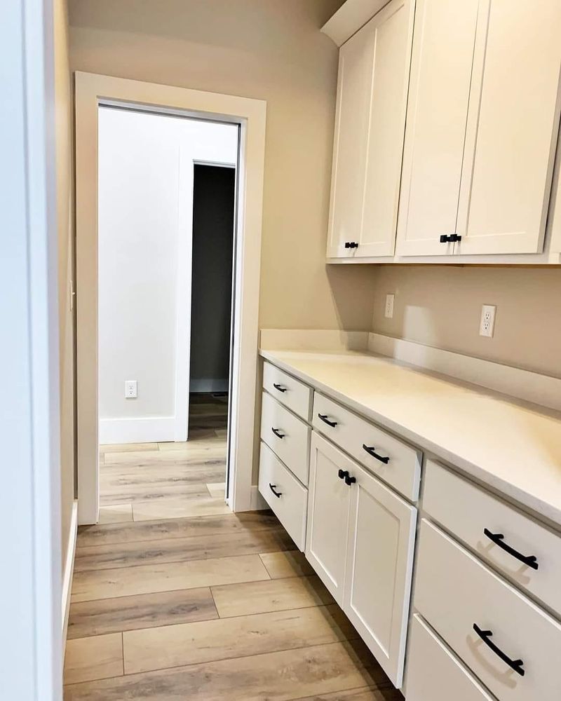 A kitchen with white cabinets and drawers and wooden floors.