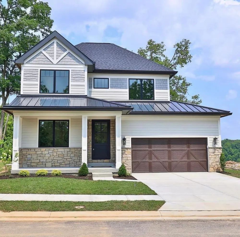 A white house with a black roof and a brown garage door