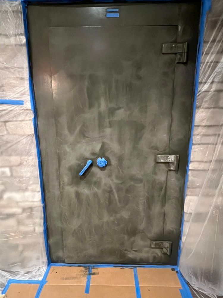 A large metal door is sitting on top of a wooden floor next to a brick wall.