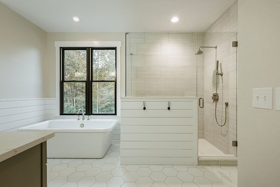 A bathroom with a tub , sink , shower and window.