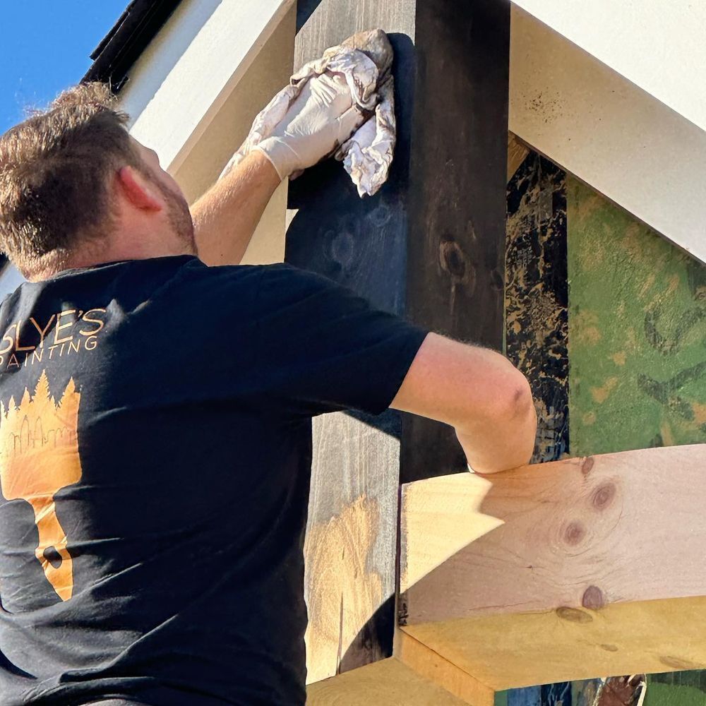 A man in a black shirt is cleaning a wooden post with a cloth.