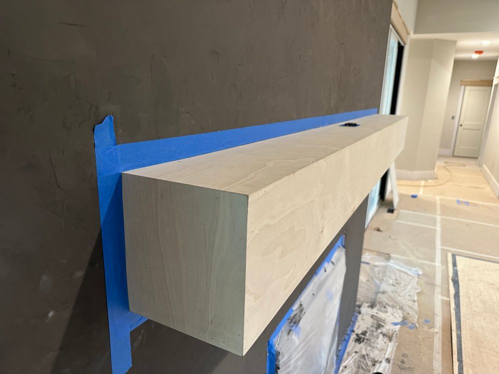 A wooden mantle is being painted on a wall with blue tape.