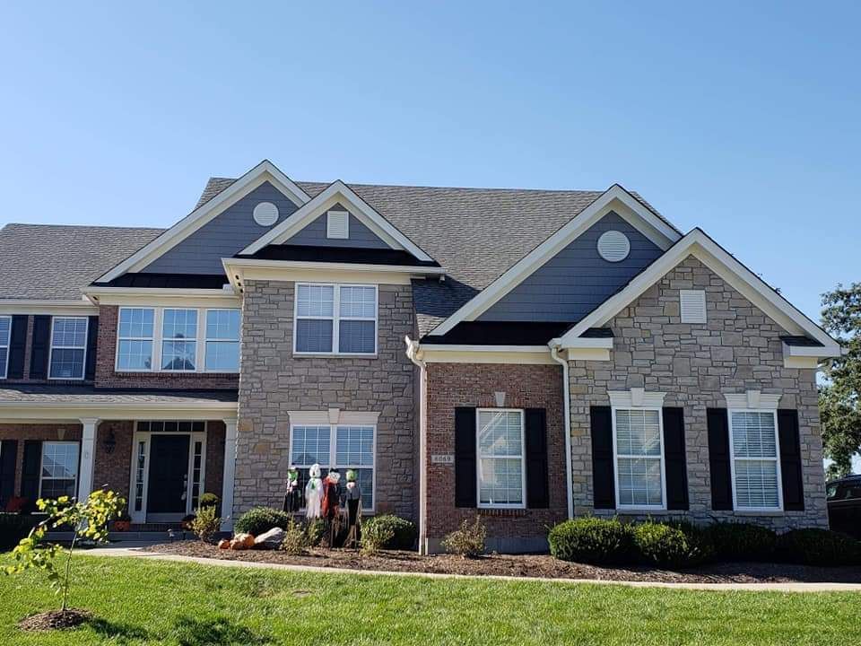 A large brick house with black shutters and a blue sky in the background.
