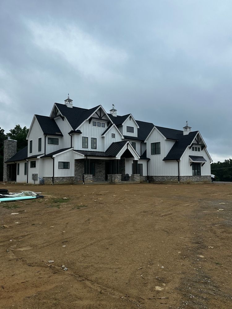 A large white house with a black roof is sitting on top of a dirt field.
