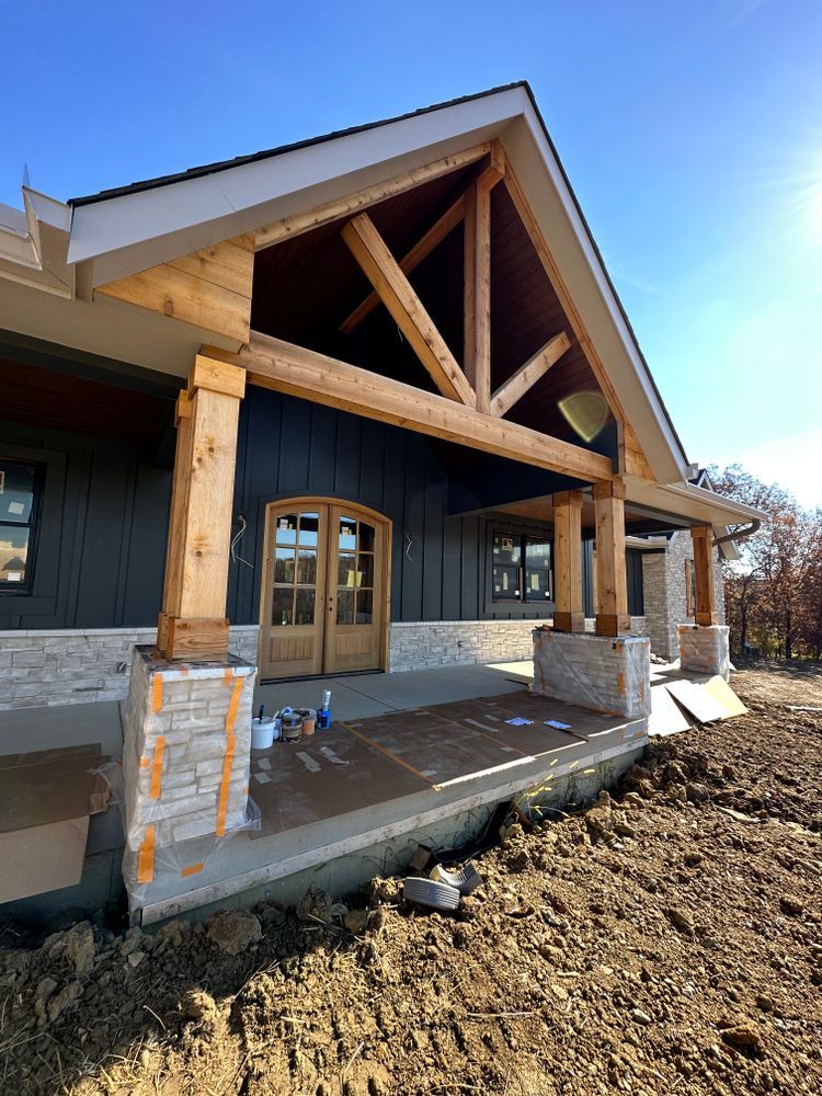 A large house with a porch and a wooden roof is being built.