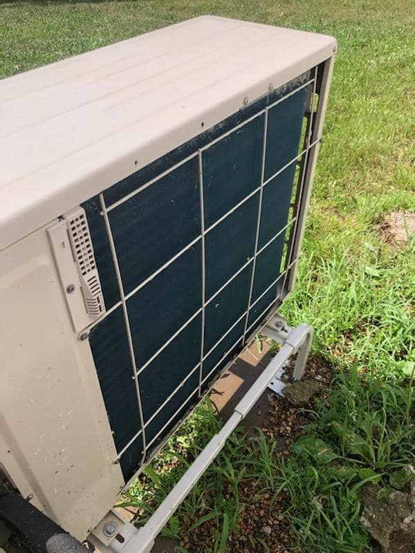 Outdoor air conditioner unit with a protective metal grid.