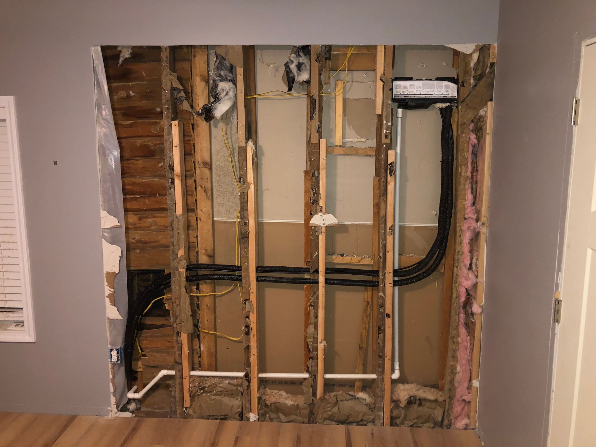 Wall opening revealing studs, pipes, electrical wires, and insulation.