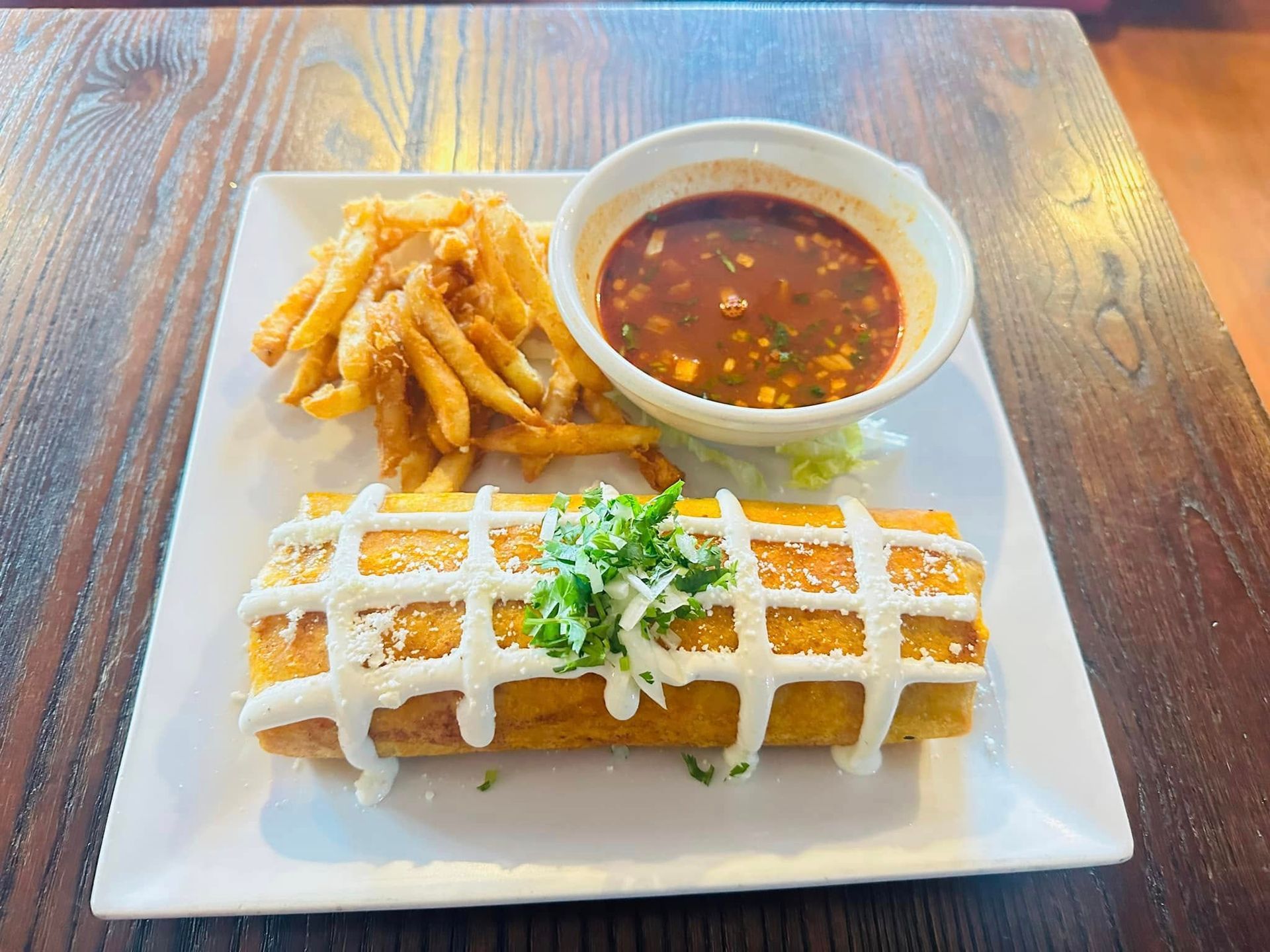 Plate of food: burrito, fries, and sauce. Burrito topped with white sauce and cilantro.