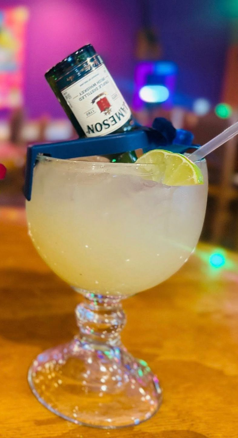 Margarita in a large glass with a Jameson bottle, lime slice, and straw.