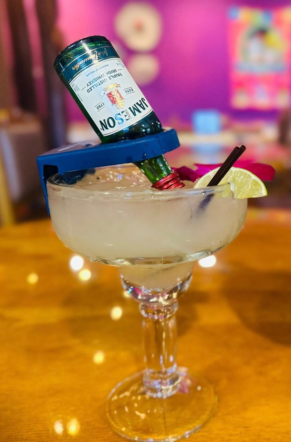 Margarita with a Jameson bottle, lime, and flower, in a colorful restaurant setting.