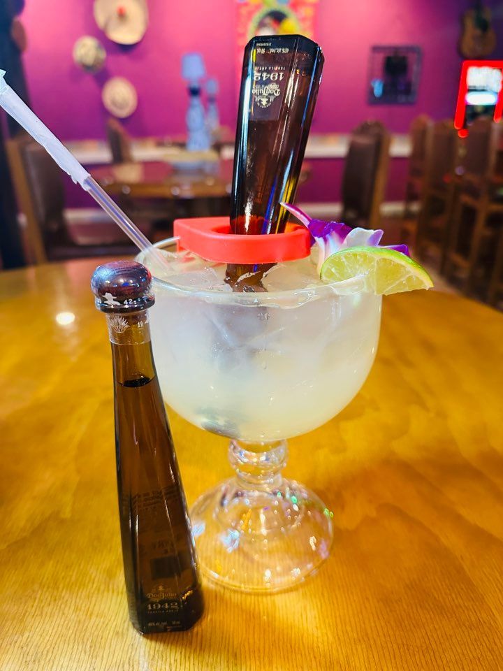 Margarita with a tequila bottle upside down in it, lime wedge, straw on a wooden table.