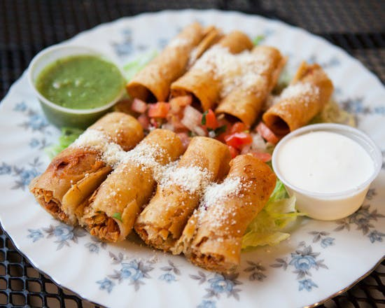 Plate of rolled tacos with salsa, sour cream, and green sauce.