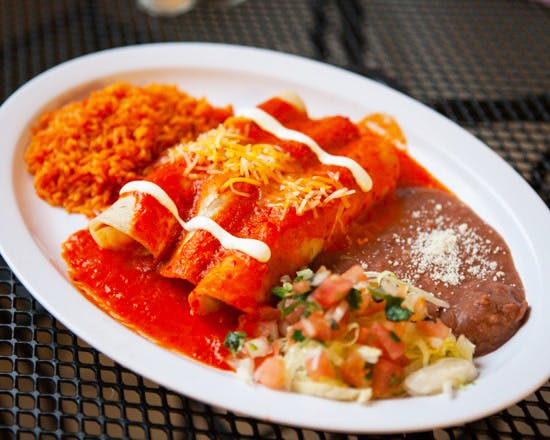 Enchiladas in red sauce with rice, beans, and pico de gallo on a white plate.