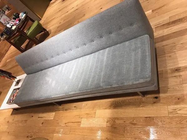 Gray futon on wooden floor, near table and green chair.
