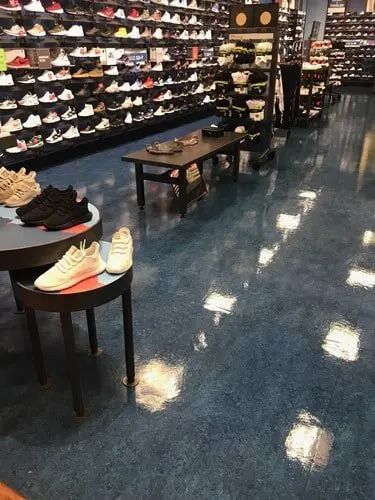 Shoe store interior with shelves of shoes, a display table, and reflective blue floor.