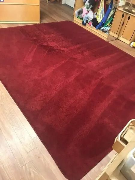 Red rectangular rug on a light wooden floor in a room. Cabinets are in the background.