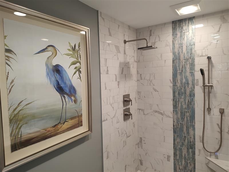 Bathroom with a heron painting, marble tile, and shower fixtures.