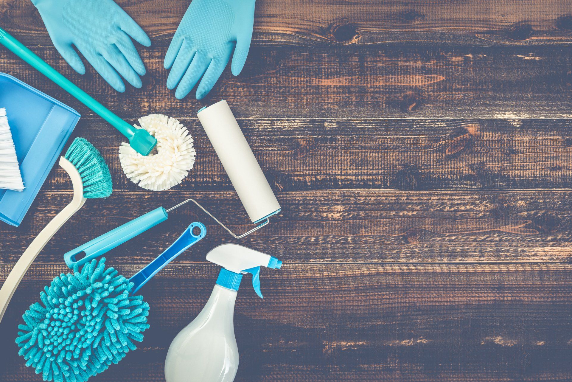 Cleaning supplies, including gloves, brushes, and spray bottle, on a wooden surface.