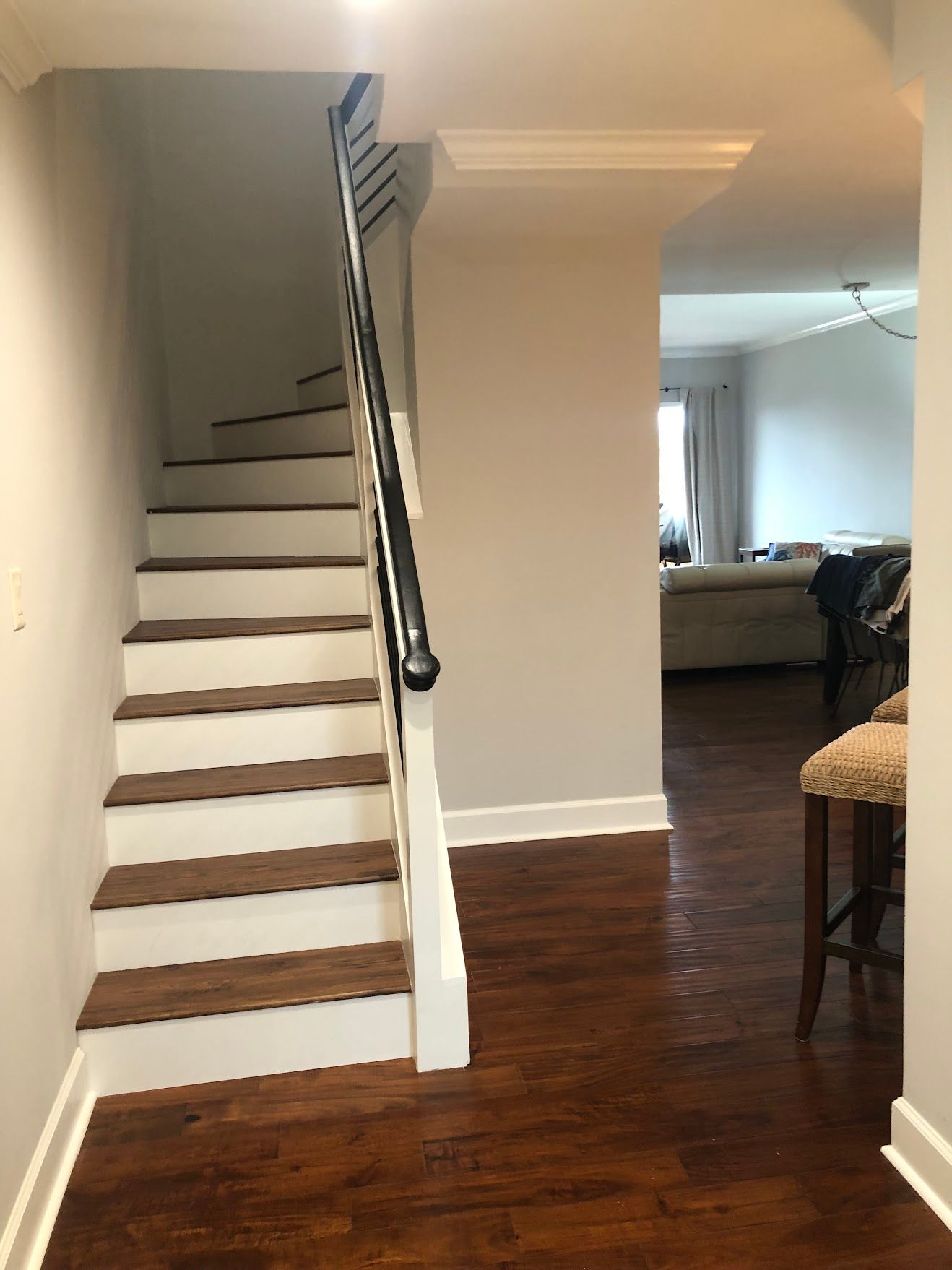 Staircase with wooden steps, white risers, and black railing. Dark wood flooring in the entry, view into living room.