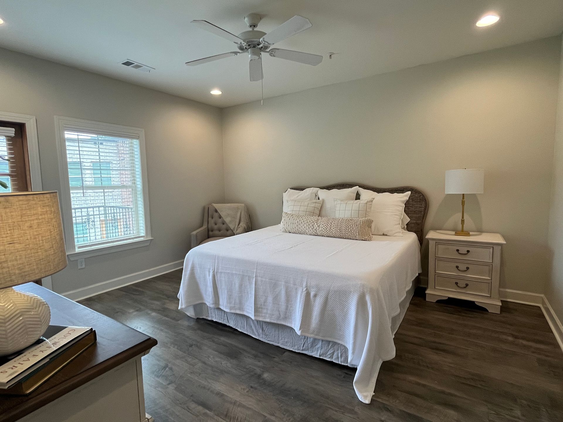 Bedroom with a bed, nightstand, chair, window, and ceiling fan. Neutral color scheme.