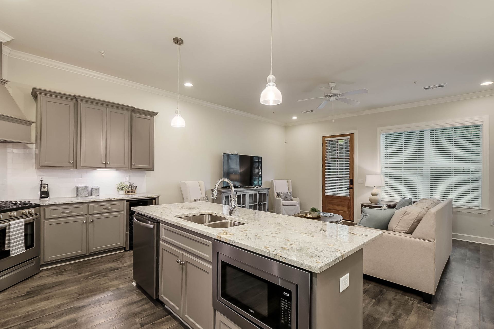 Open-concept kitchen and living area with gray cabinets, island, stainless steel appliances, and a light-colored sofa.