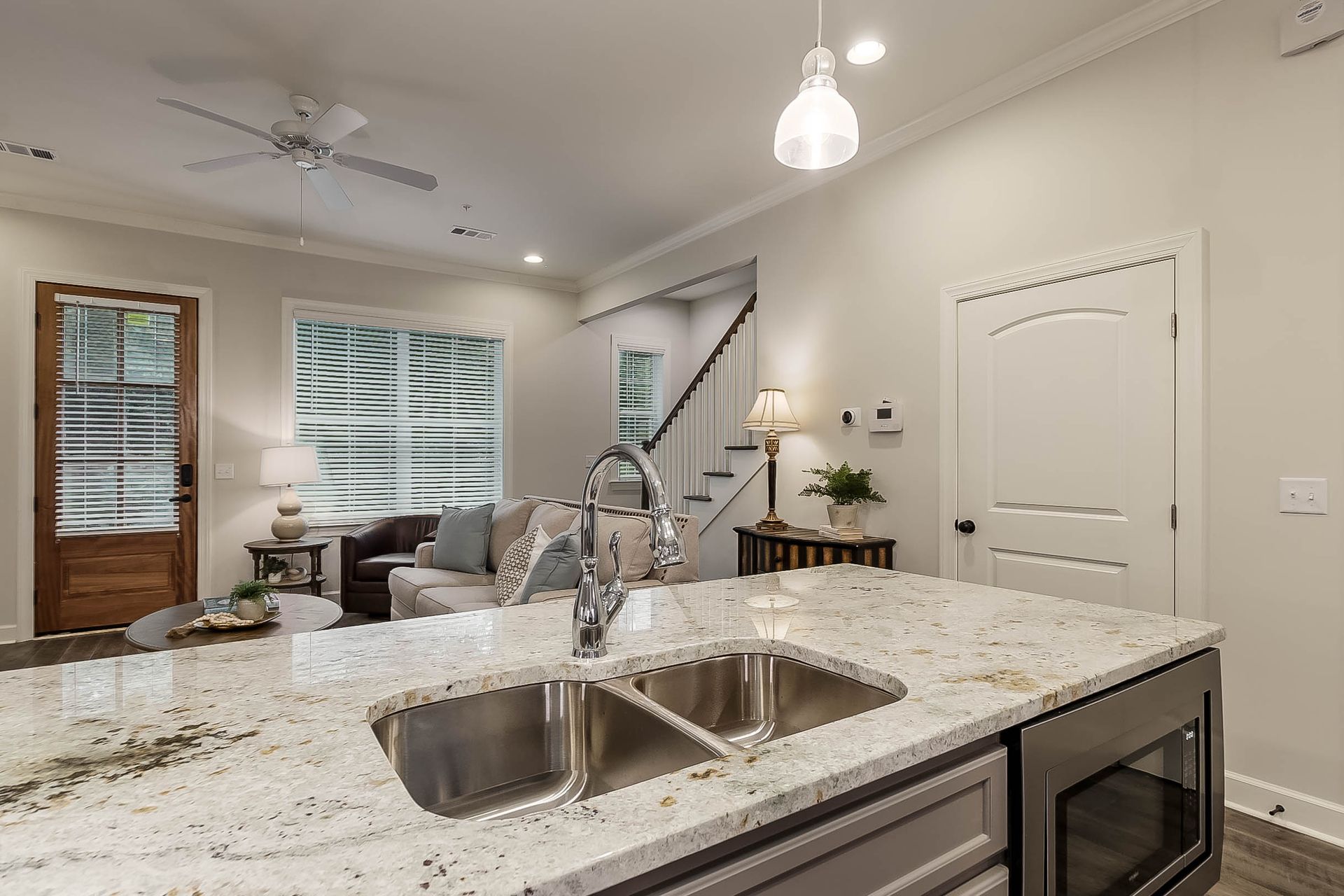 Kitchen island with a sink, overlooking a living room with a couch, windows, and a staircase.