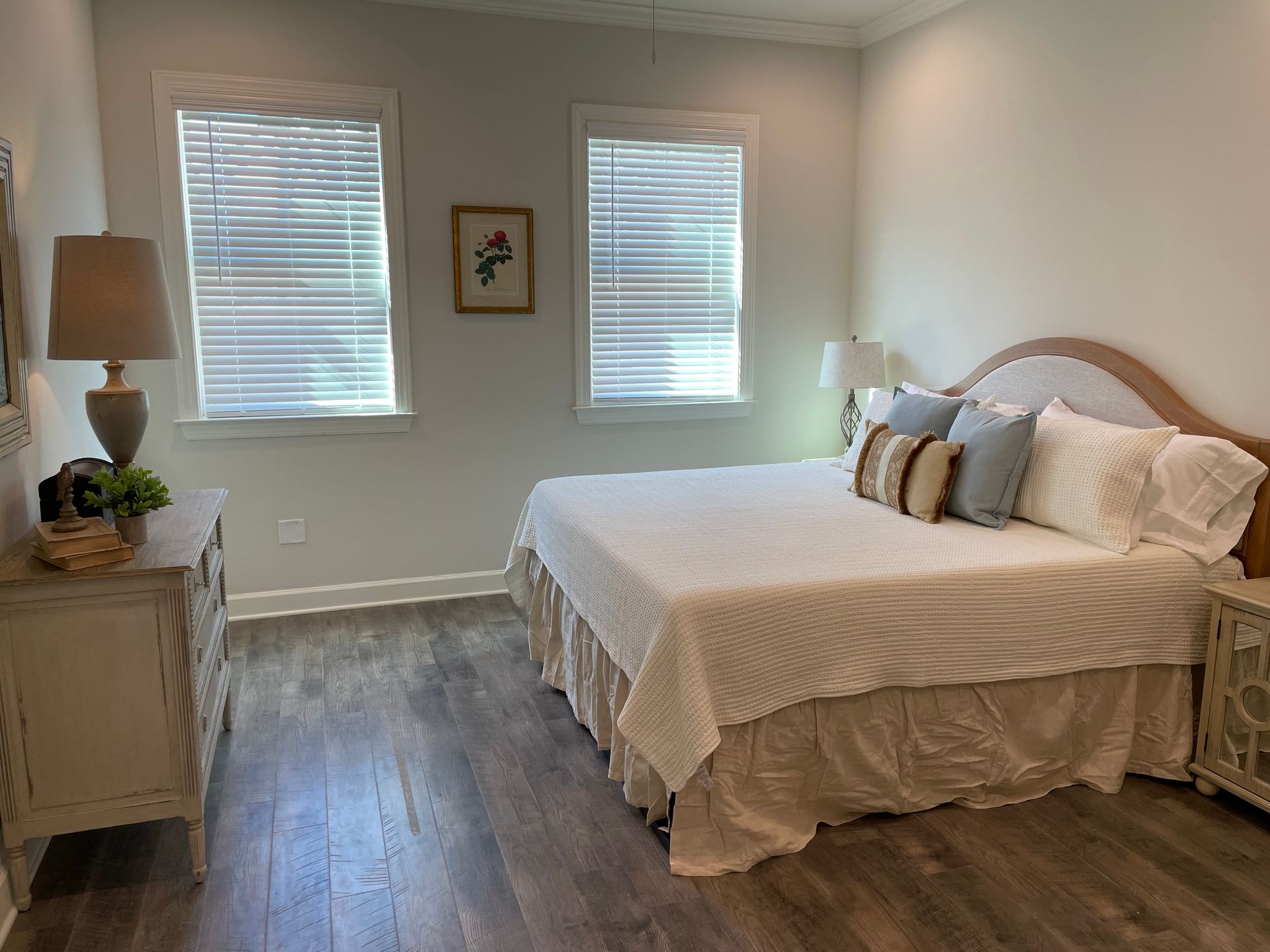 Bedroom with a bed, dresser, windows with blinds, and hardwood floors.