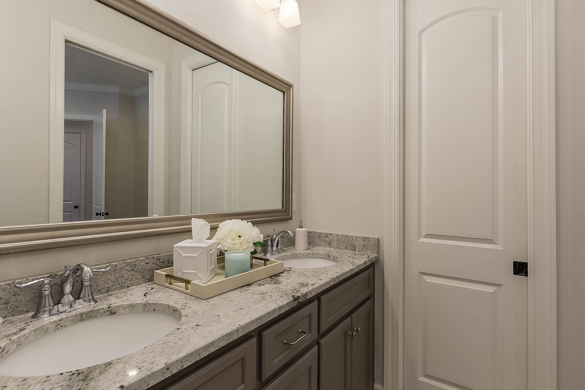 Bathroom with double sinks, large mirror, and gray granite countertop. White walls and door.