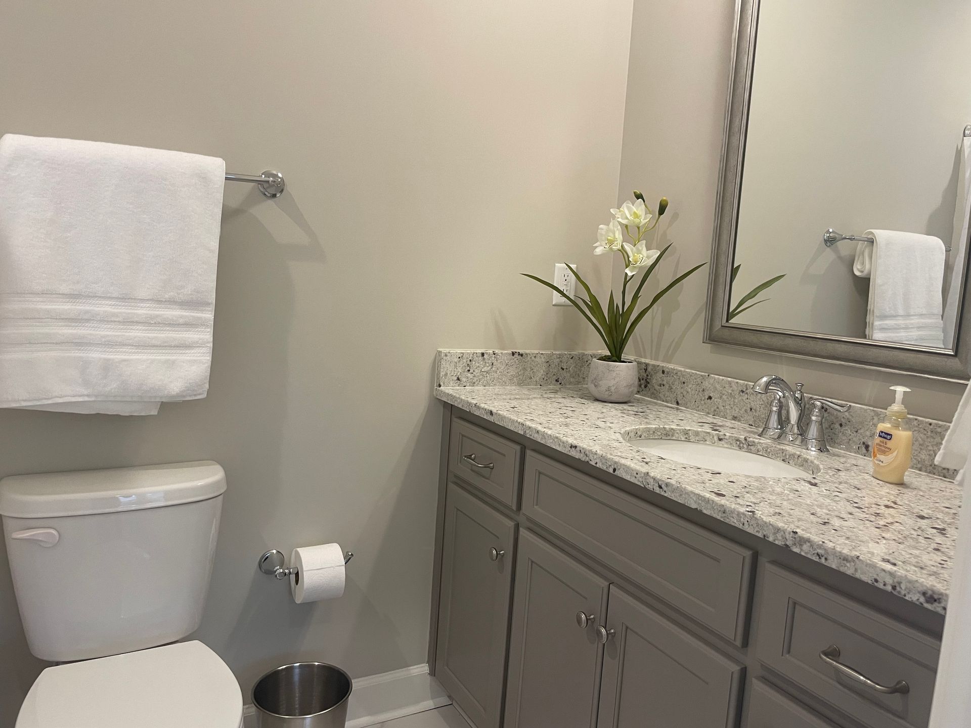 Bathroom with white toilet, gray vanity, and white towel. Silver mirror and fixtures.