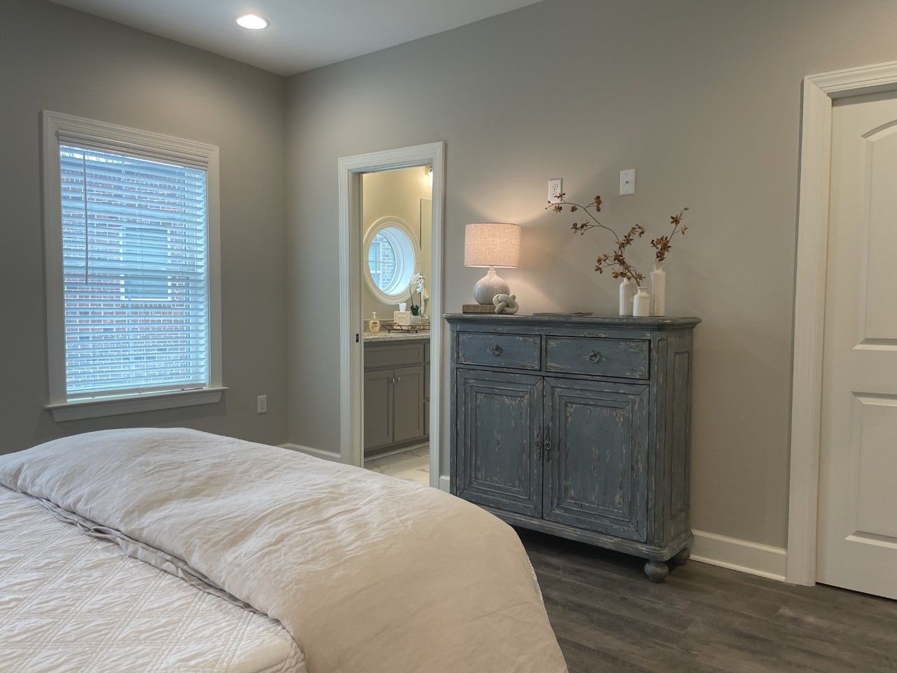 Bedroom with gray walls, bed, blue cabinet, doorway to bathroom, and window with blinds.