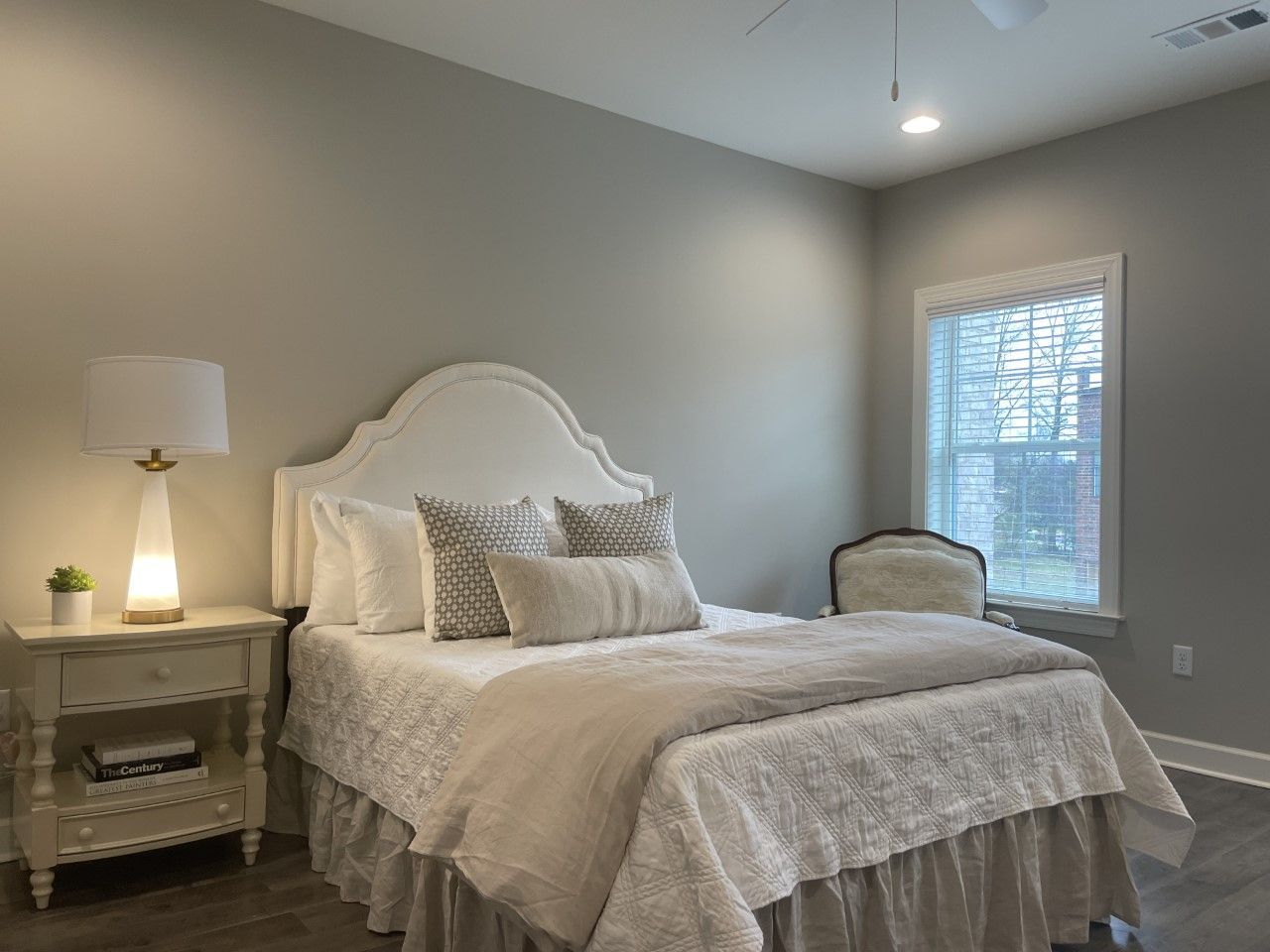 Bedroom with white bed, beige walls, nightstand, and small window.