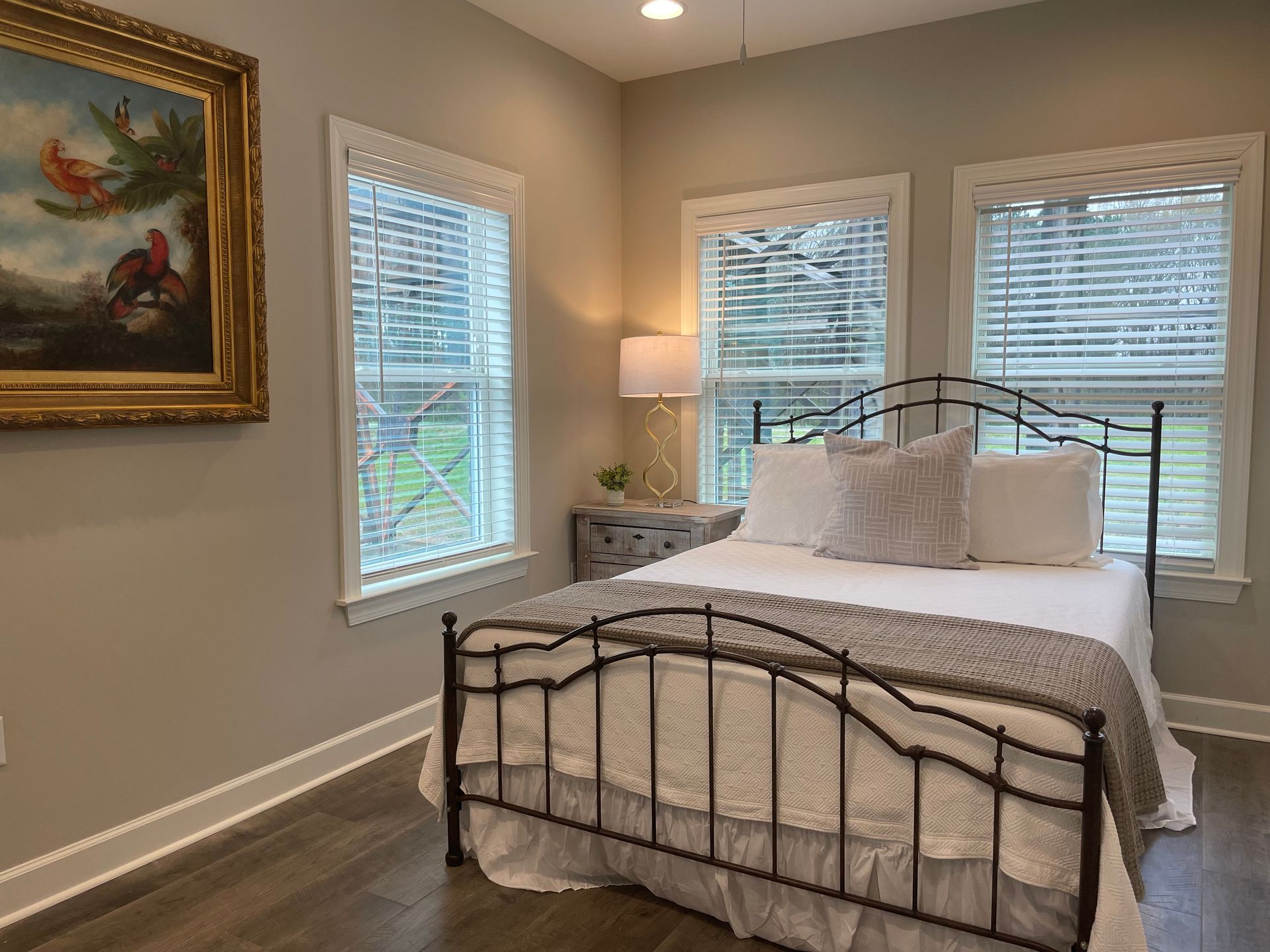 Bedroom with a black metal bed frame, three windows with blinds, and artwork on the wall.