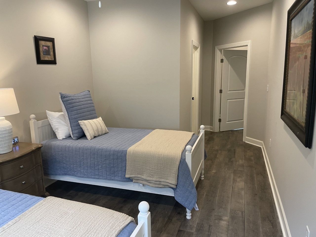 Two beds with blue and tan bedding in a bedroom with wooden floors and a hallway.