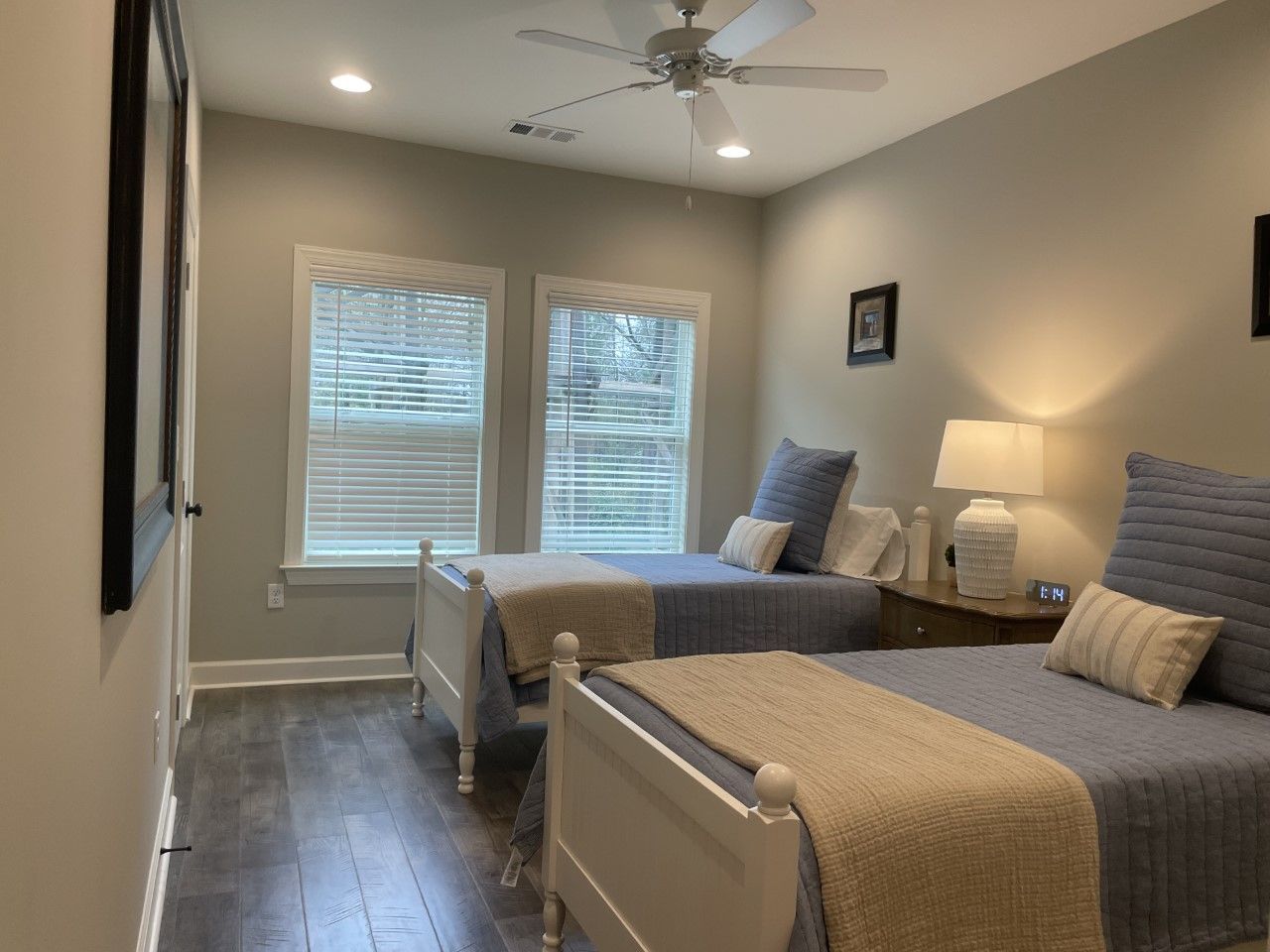 Bedroom with two twin beds, blue quilts, white frames, beige blankets, and a ceiling fan.