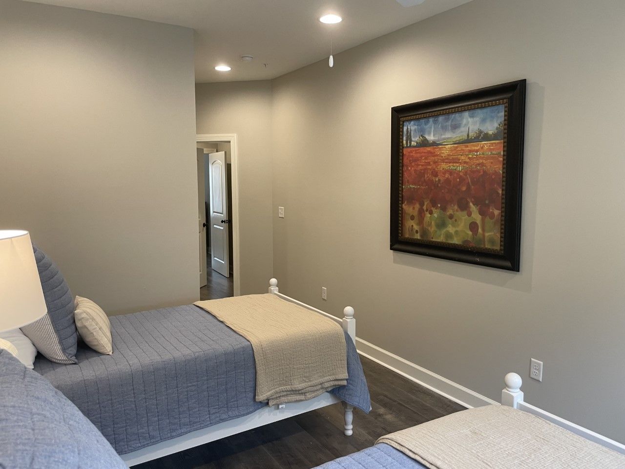 Bedroom with two twin beds, gray walls, artwork, and an open doorway.