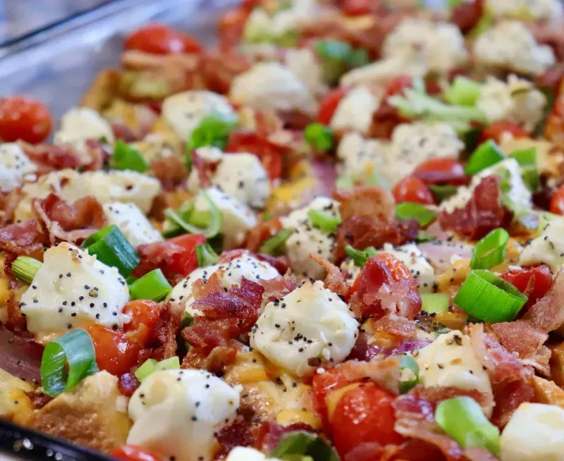 A casserole dish filled with tomatoes , cheese , bacon and green onions.