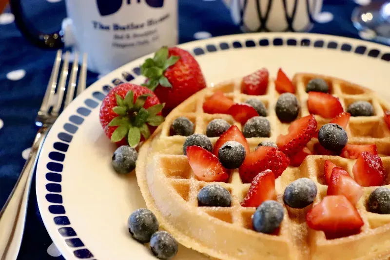 A waffle with strawberries and blueberries on a plate with a fork.