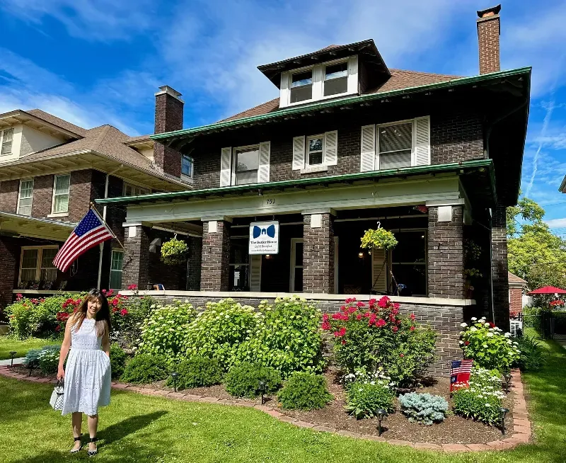 A woman in a white dress is standing in front of a large house.
