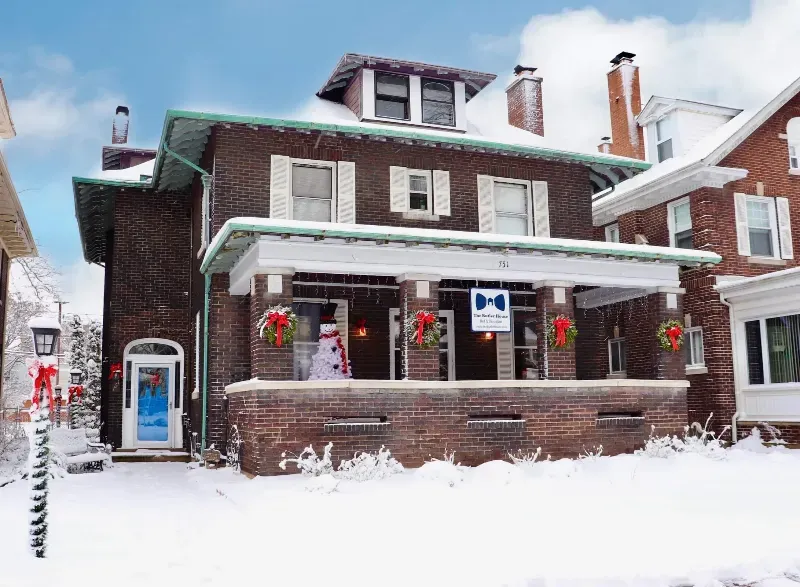 A brick house with a porch decorated for christmas is covered in snow.