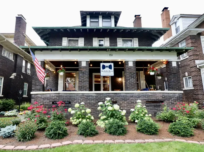 A large brick house with a large porch and flowers in front of it.