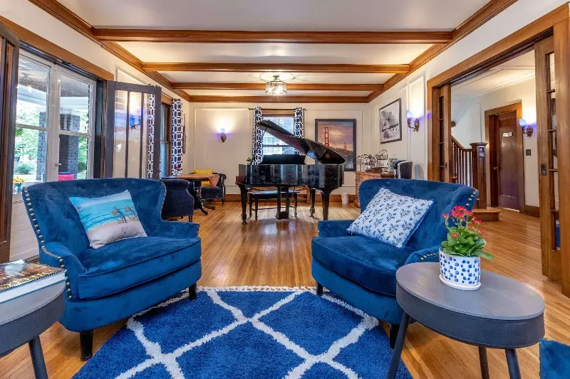 A living room with blue chairs and a piano.